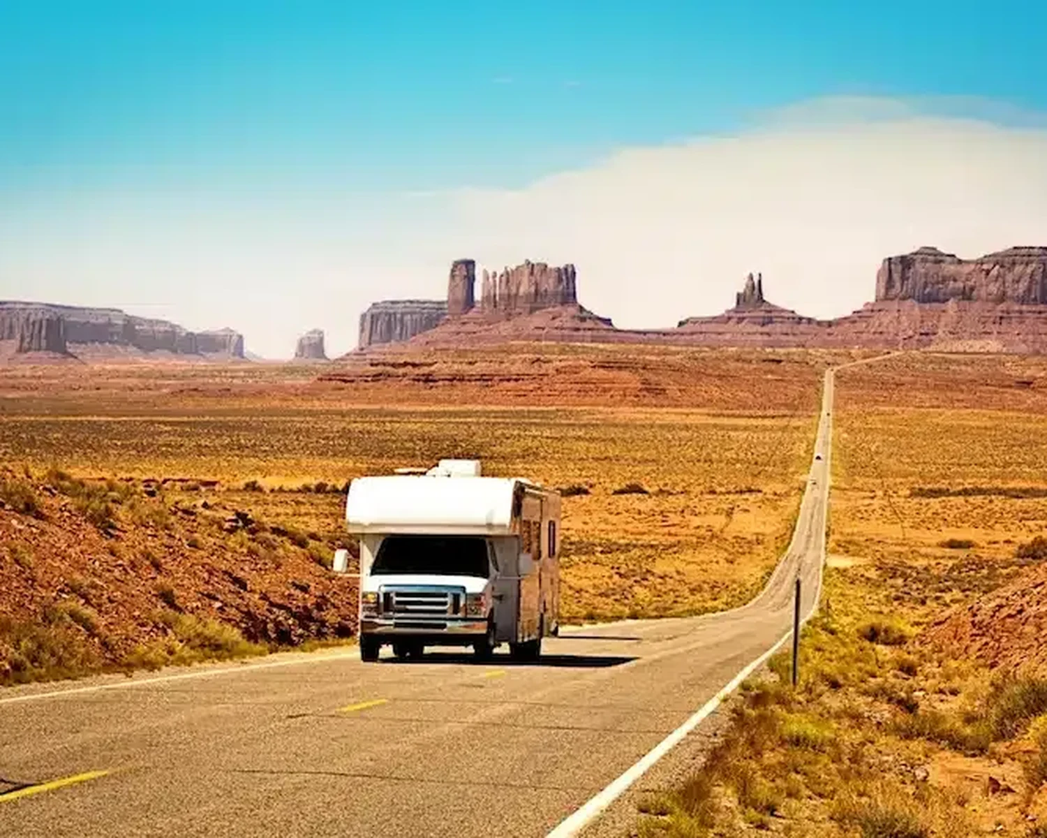 Um motorhome Classe C em uma rodovia no deserto, rumo aos morros de rocha vermelha do sudoeste americano